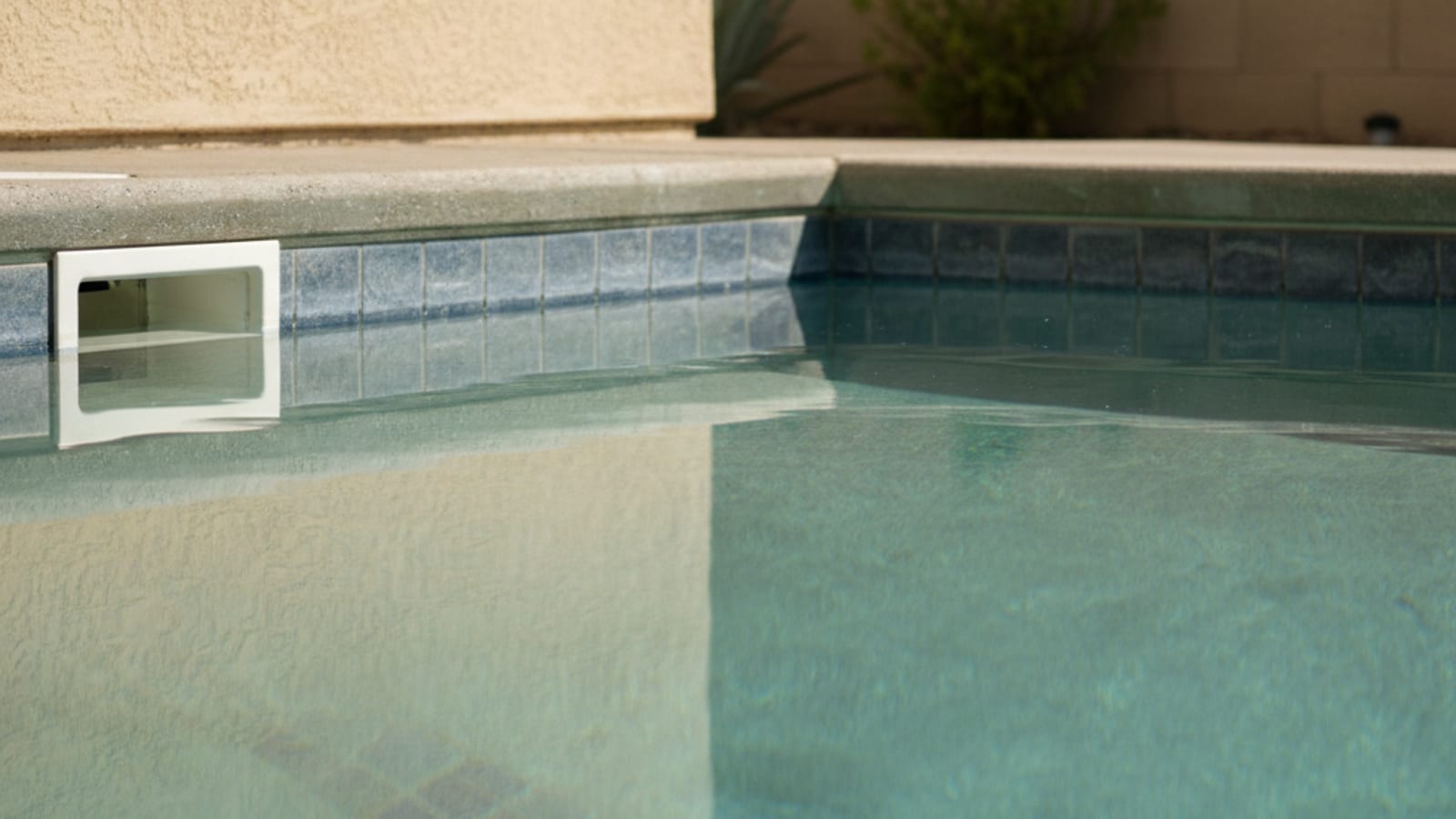 Close-up of cloudy hazy pool water showing reduced visibility with a pool skimmer and tiled edge